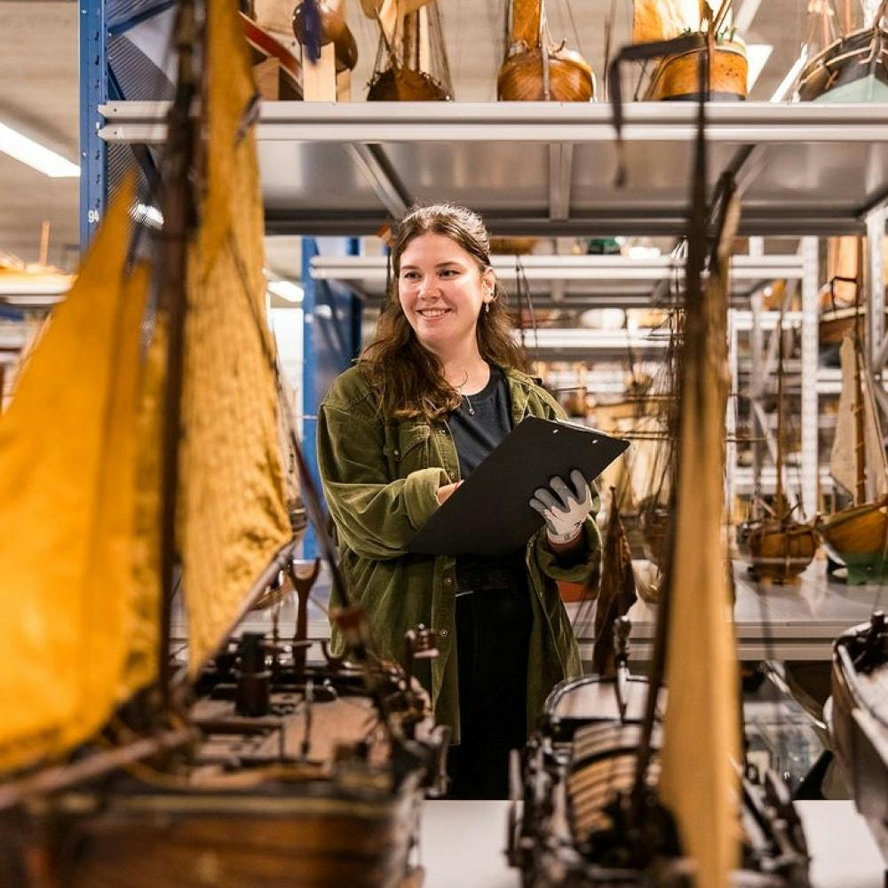 Een persoon glimlacht en maakt aantekeningen in het Scheepvaart Museum in Amsterdam