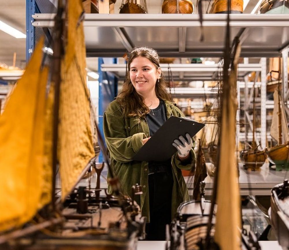 Een persoon glimlacht en maakt aantekeningen in het Scheepvaart Museum in Amsterdam