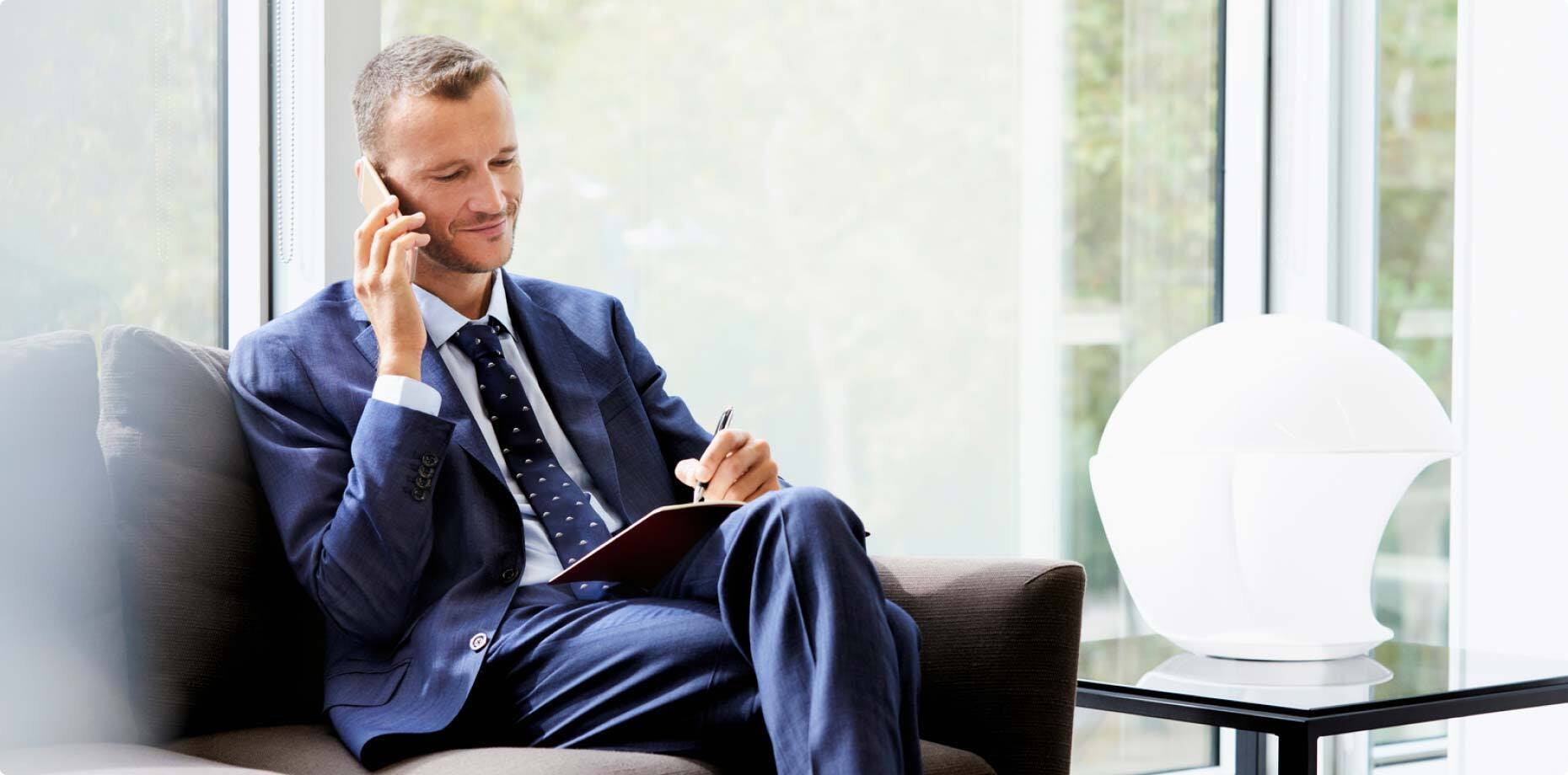 A person in work attire, sitting on a sofa and talking on the phone